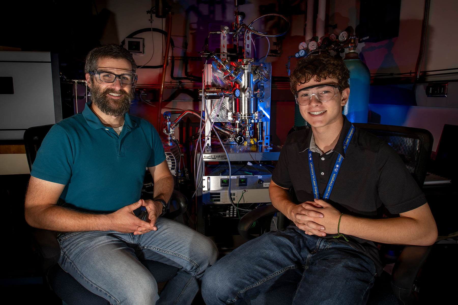 A researcher and a student wearing safety glasses sitting in front of laboratory equipment.