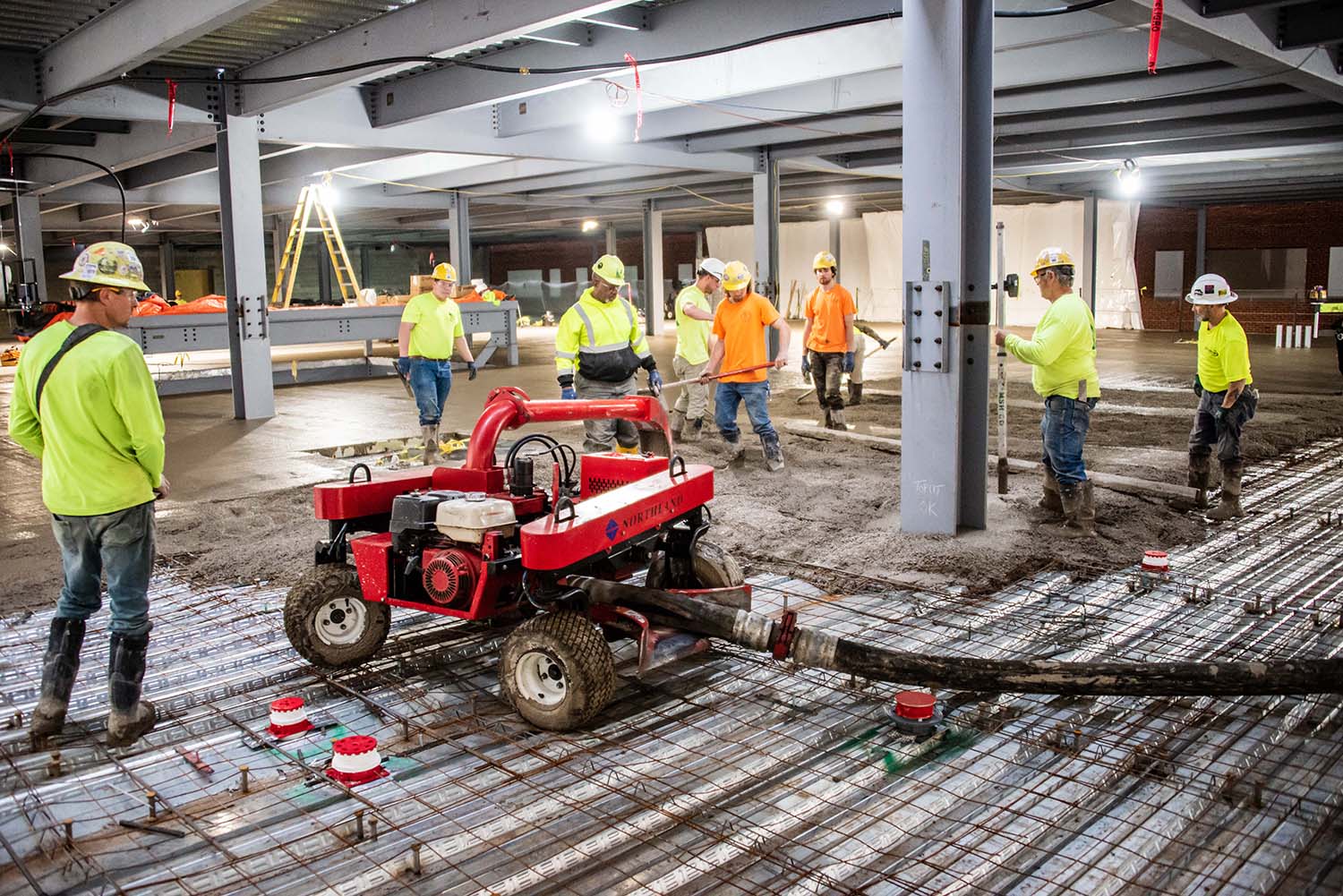 Construction workers inside with equipment spreading cement along the ground.