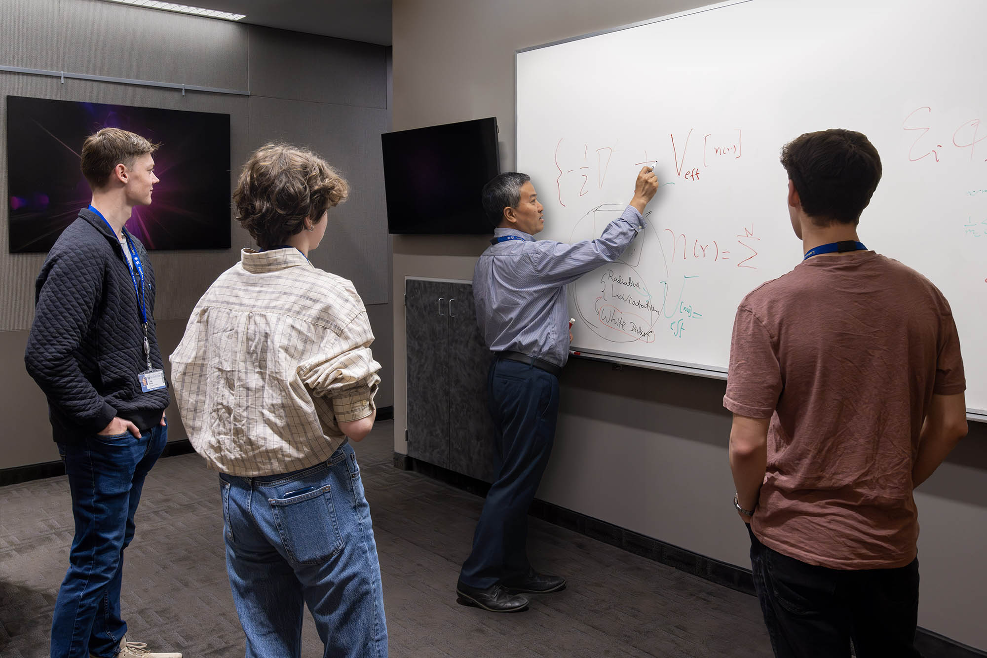 Researcher explaining a concept to students by writing an equation on a white board.