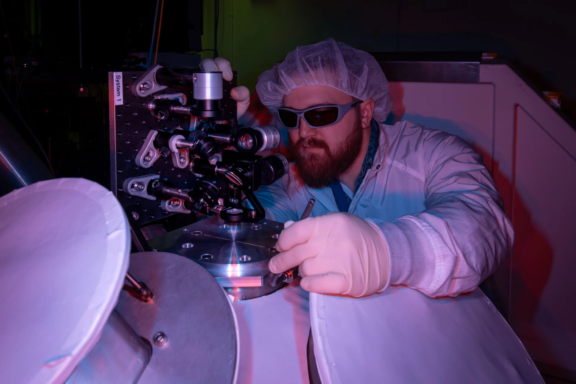 Gerrit Bruhaug working in a laboratory, wearing safety equipment, bathed in purple light.