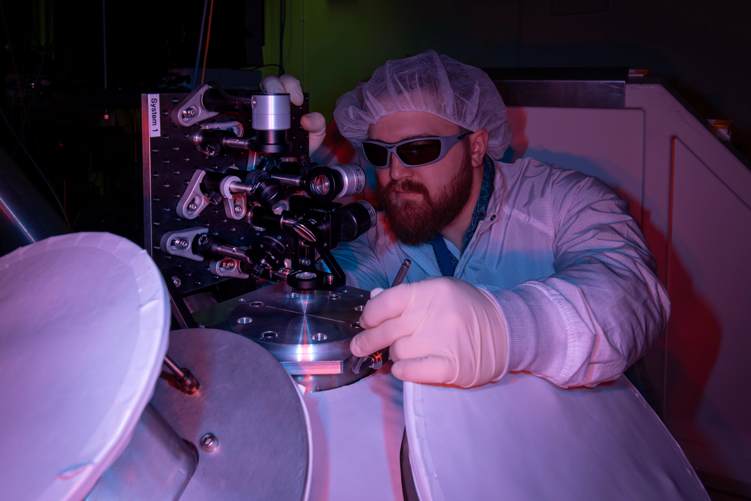 Gerrit Bruhaug working in a laboratory, wearing safety equipment, bathed in purple light.