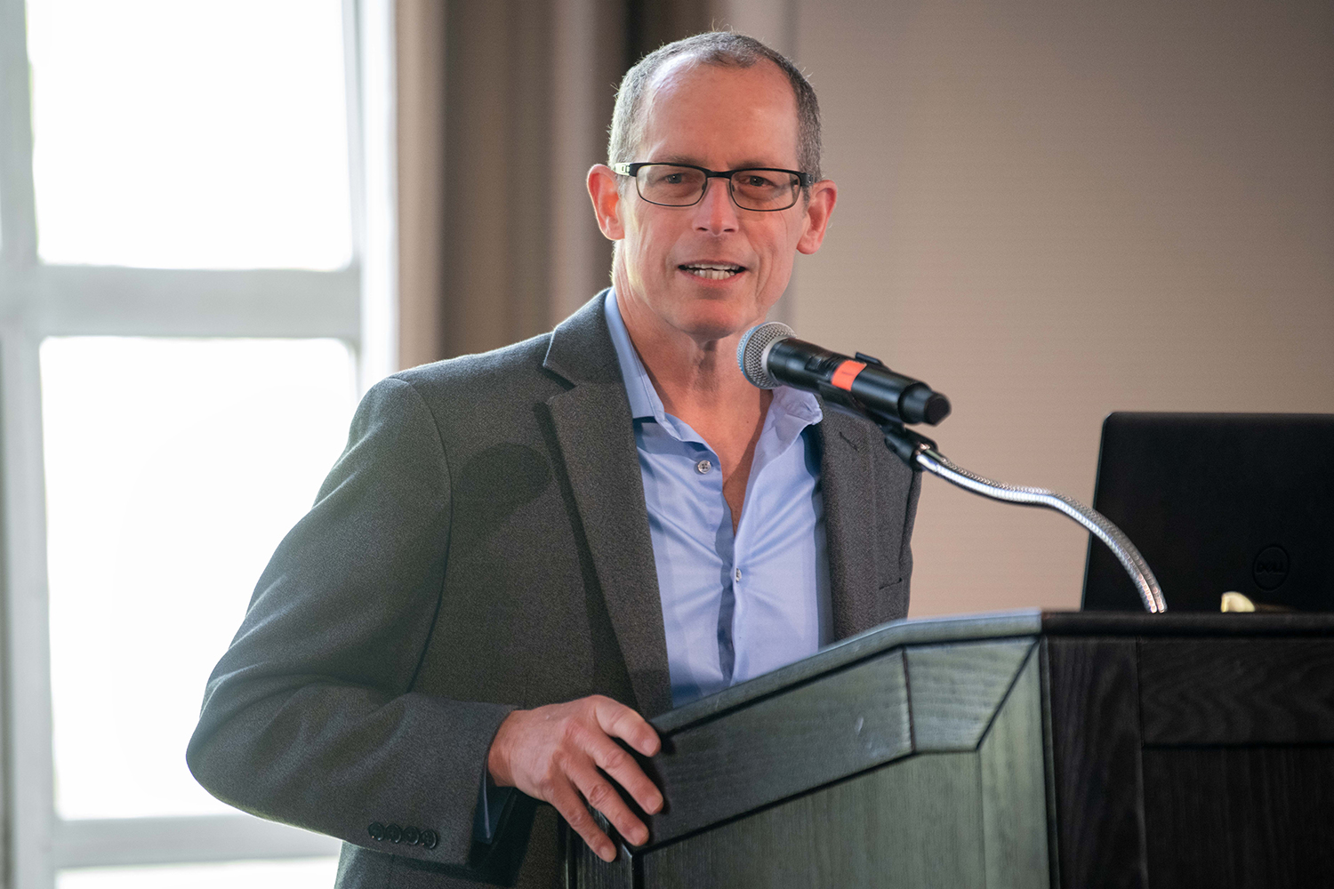 Rip Collins speaking at a podium in the University of Rochester's Douglas Commons building.