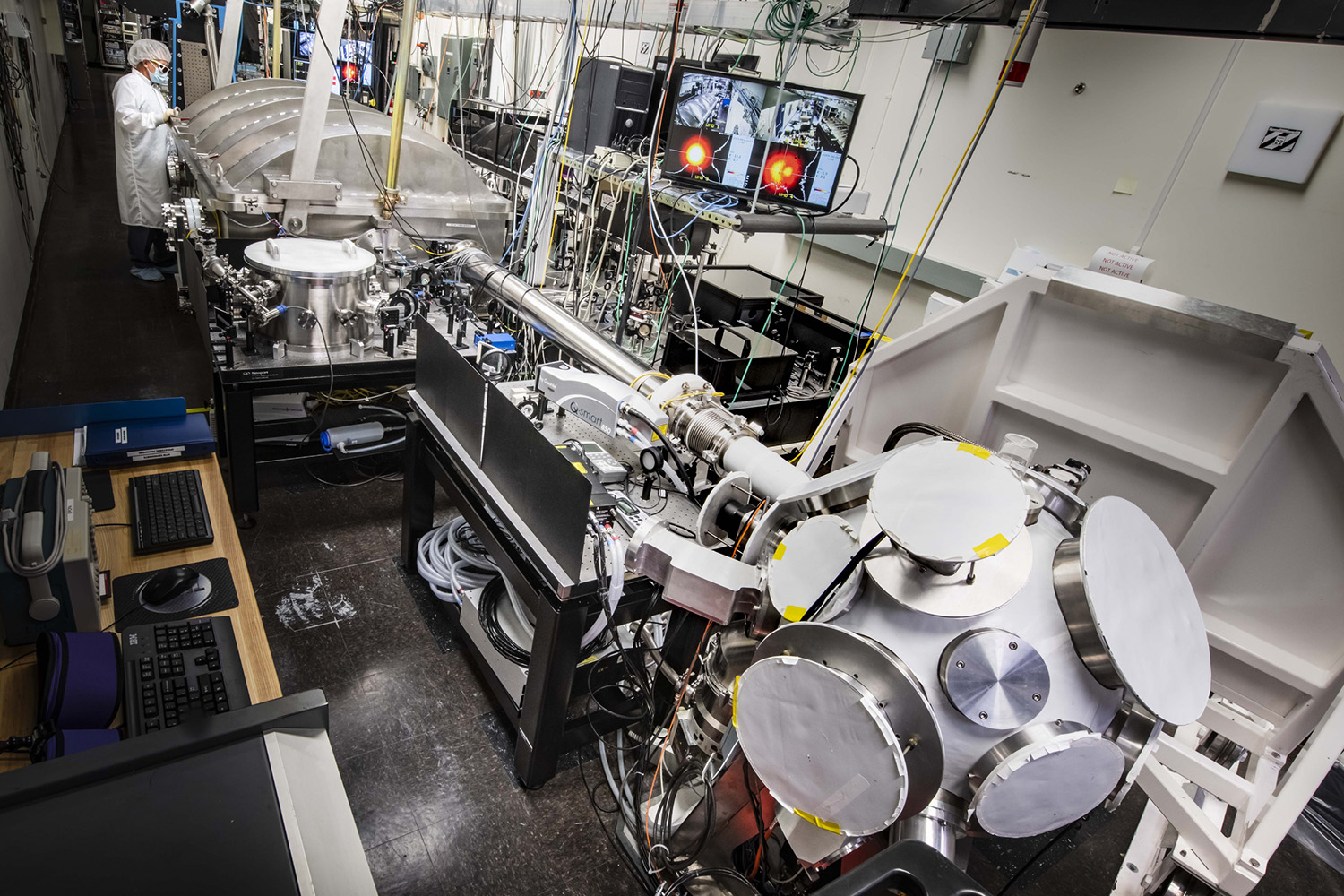 Feature image Photograph of MTW target chamber in the foreground and researcher in clean room gear in the top left background.