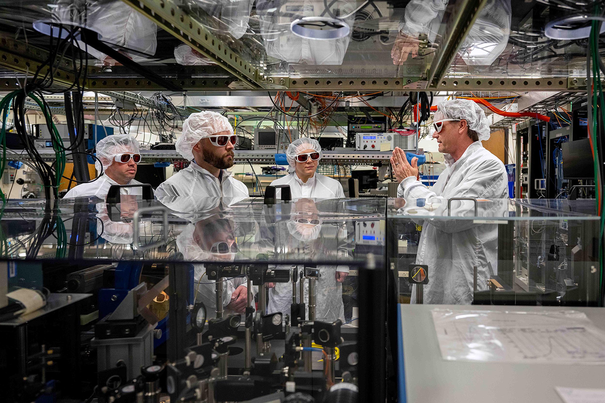 Four researchers in cleanroom attire in a laboratory.