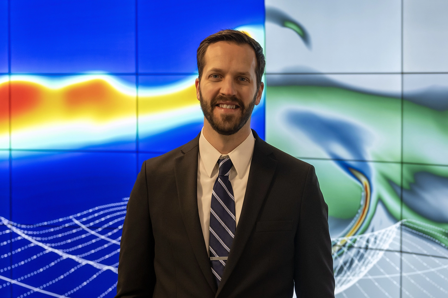 Scientist standing in front of simulation rendering on a large display of screens.