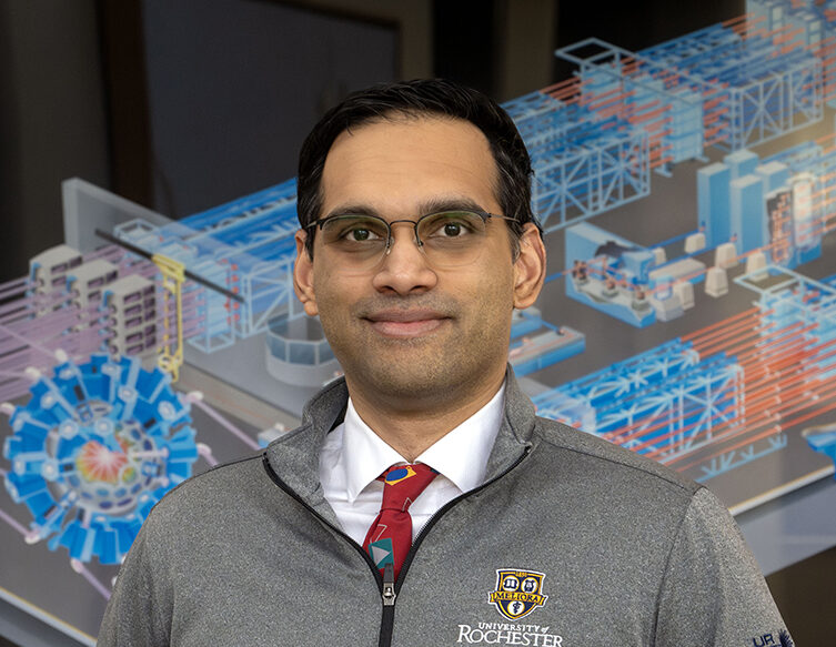 Varchas Gopalaswamy standing in front of painting of the OMEGA Laser System.