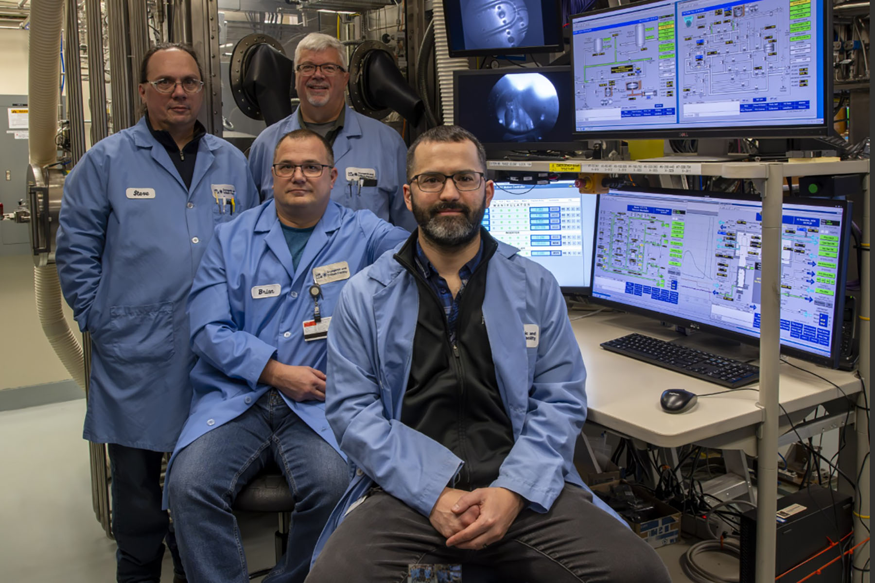 Group photo of the Cyro Fill Systems Group in lab attire next to computers and lab equipment.