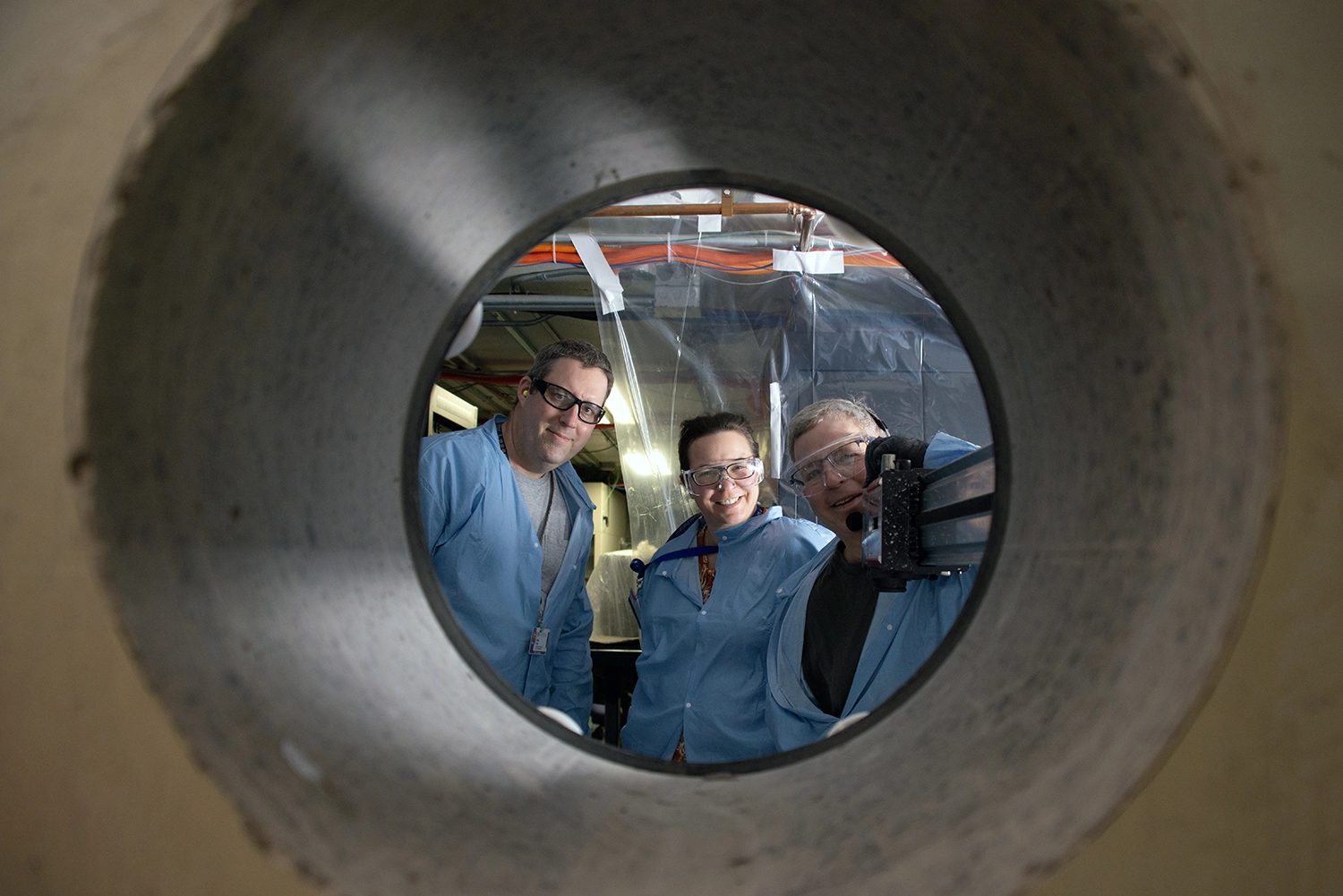 Feature image Three researchers looking through a drilled hole in the wall.