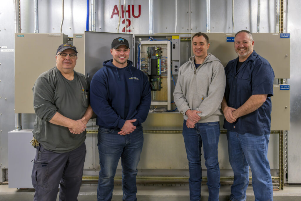 4 LLE Facilities team members in front of a systems panel.