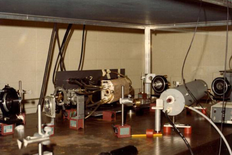 Optical table holding a series of mechanical and diagnostic components arranged for a laser or plasma experiment inside a lab.