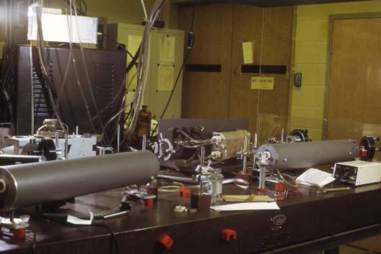 Optical laboratory bench filled with mirrors, mounts, diagnostic instruments, and cabling arranged for an experimental setup.