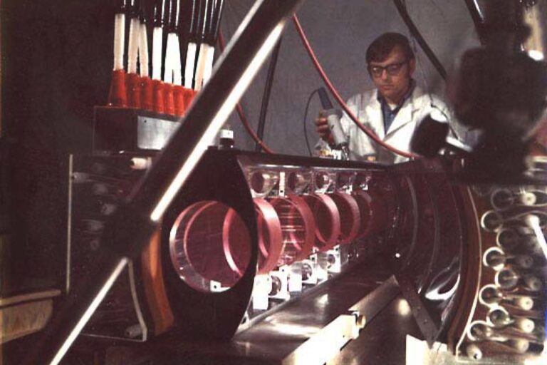 Researcher working with a long row of optical components and red-colored cylindrical mounts aligned on an optical table.