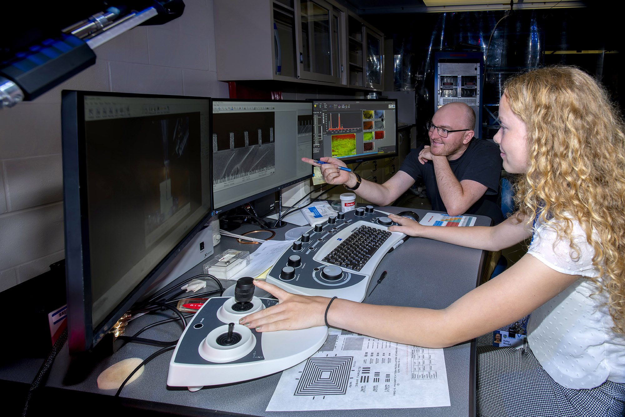 Two people at a target metrology workstation.