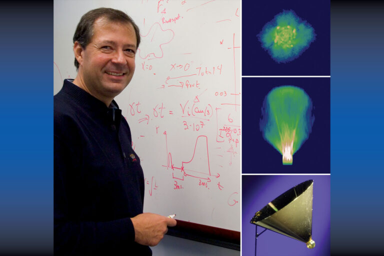 Photo of a man in casual dress standing in front of a white board which contains mathematical equations.