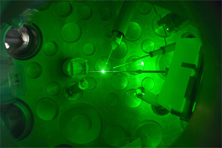 Photo of multiple laser beams converging toward a bright burst within a laser target bay.