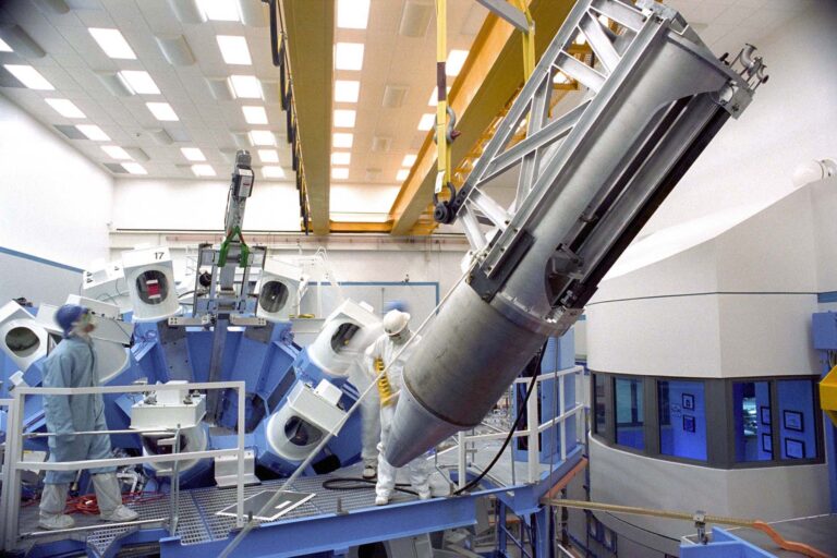 Photo of technicians in cleanroom suites and helmets overseeing the installation of a spectrometer in a laser bay.