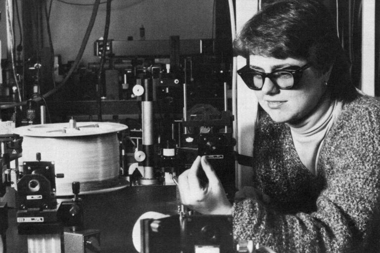 Photo of a researcher using optical equipment, wearing protective eyewear and adjusting components on a laboratory table.