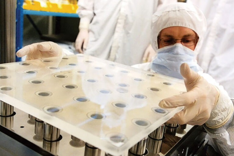 A photo person in lab cleanroom attire handling a piece of equipment.