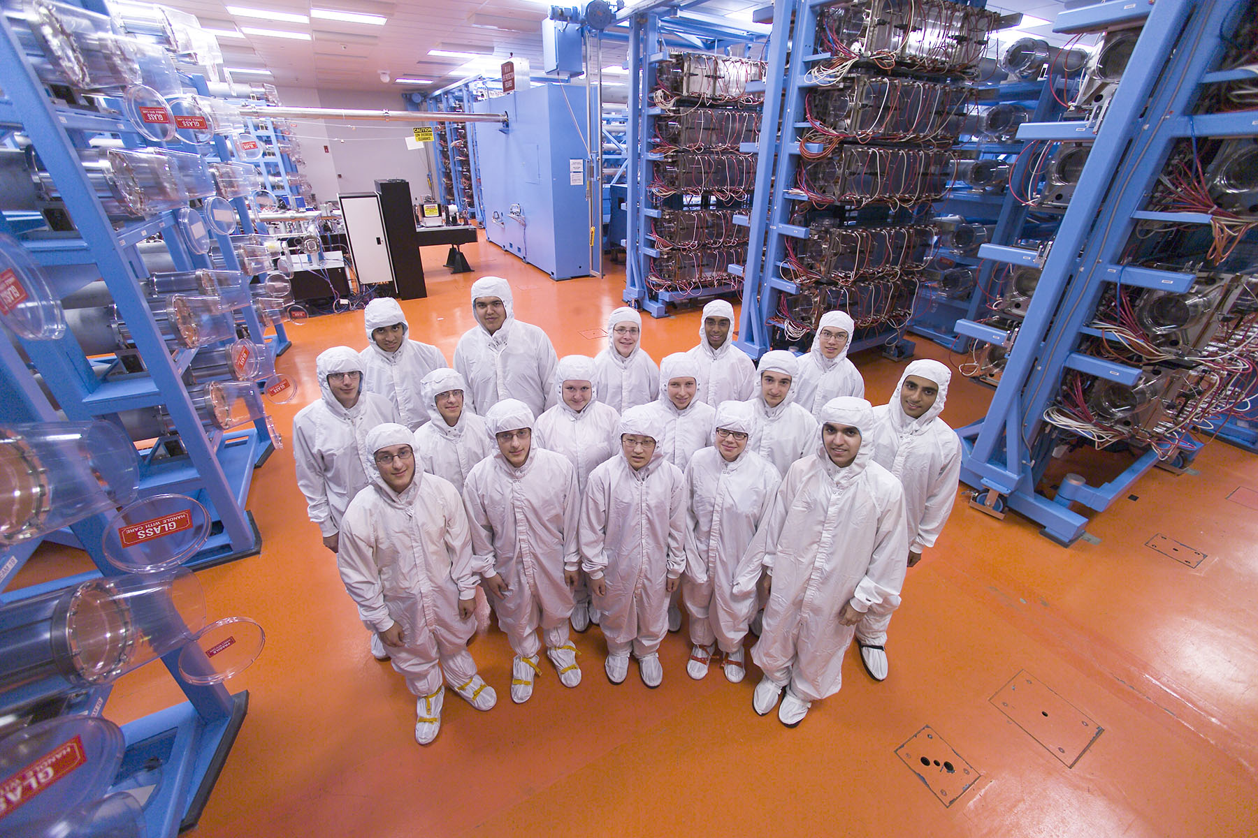Group of high school students are pictured wearing white cleanroom suits inside the LLE laser bay.