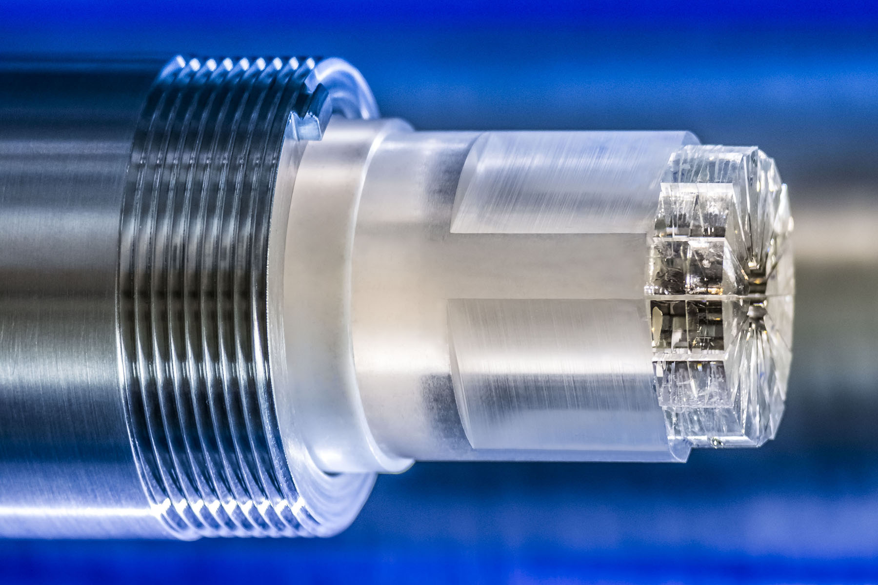 A close-up photo of a metallic cylindrical scientific component with precision threads and internal structures.