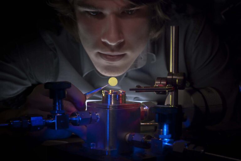 Photo of a scientist or technician in a darkened room intensely examining and preparing an illuminated membrane which is held by an instrument resembling small pliers.