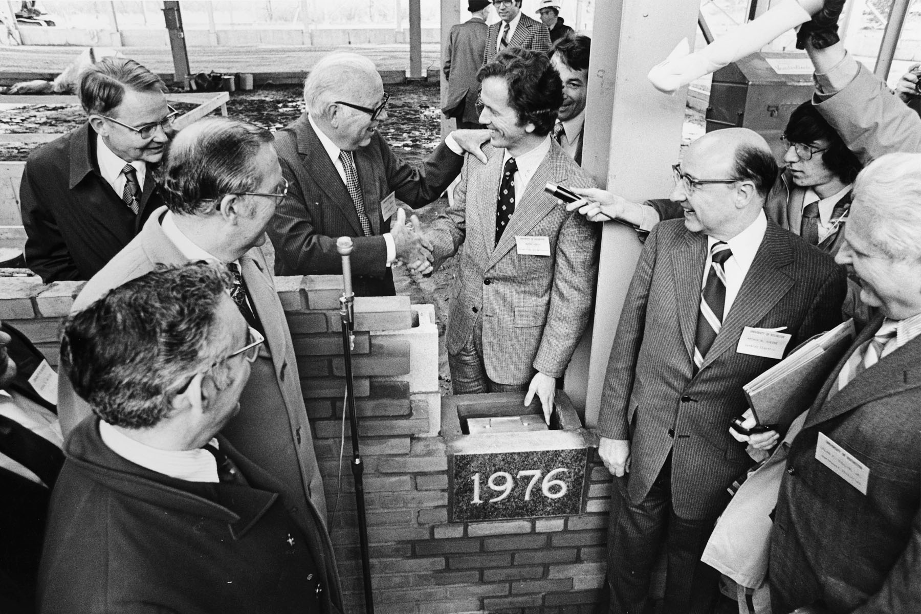 Black-and-white photograph of people gathered around the 1976 cornerstone as it is set into place during construction of the Laboratory for Laser Energetics building.
