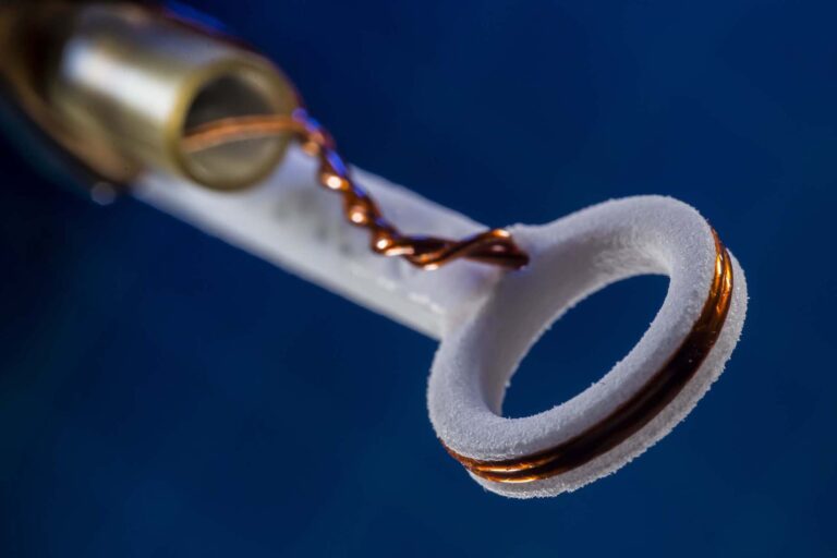 Close-up of a small experimental target mount with coiled wire and a circular ceramic holder used in high-precision laser research.