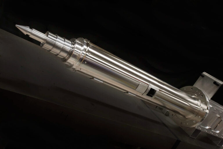 Highly polished metal cylindrical laser component, set against a dark background.