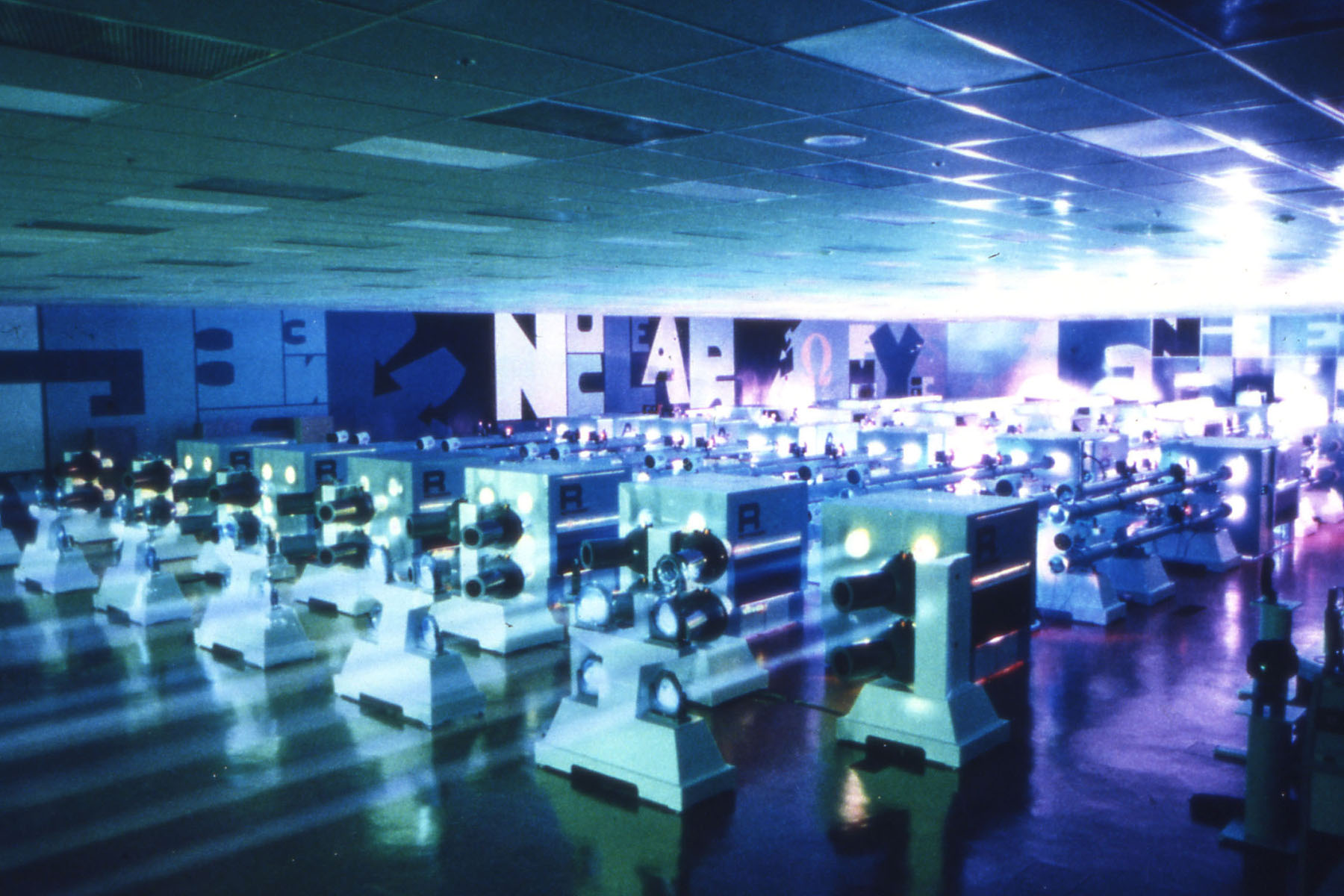 Historic photo of a laser facility hall filled with rows of large green laser beamline components illuminated by blue lighting.