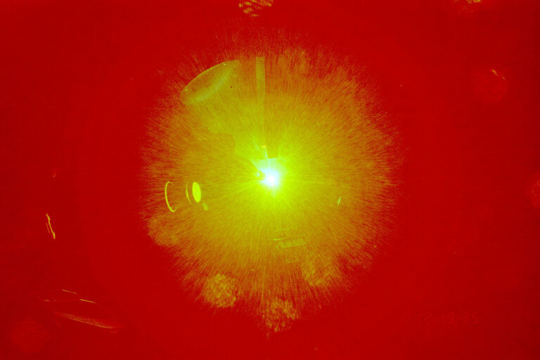 A bright green laser beam illuminating a red plasma-like burst, captured during a high-energy laser experiment.