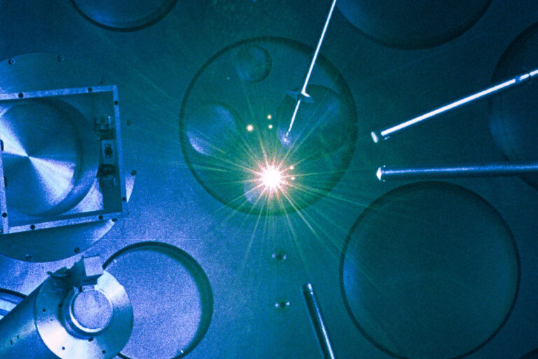 Photo of multiple laser beams converging toward a bright burst within a laser target bay.