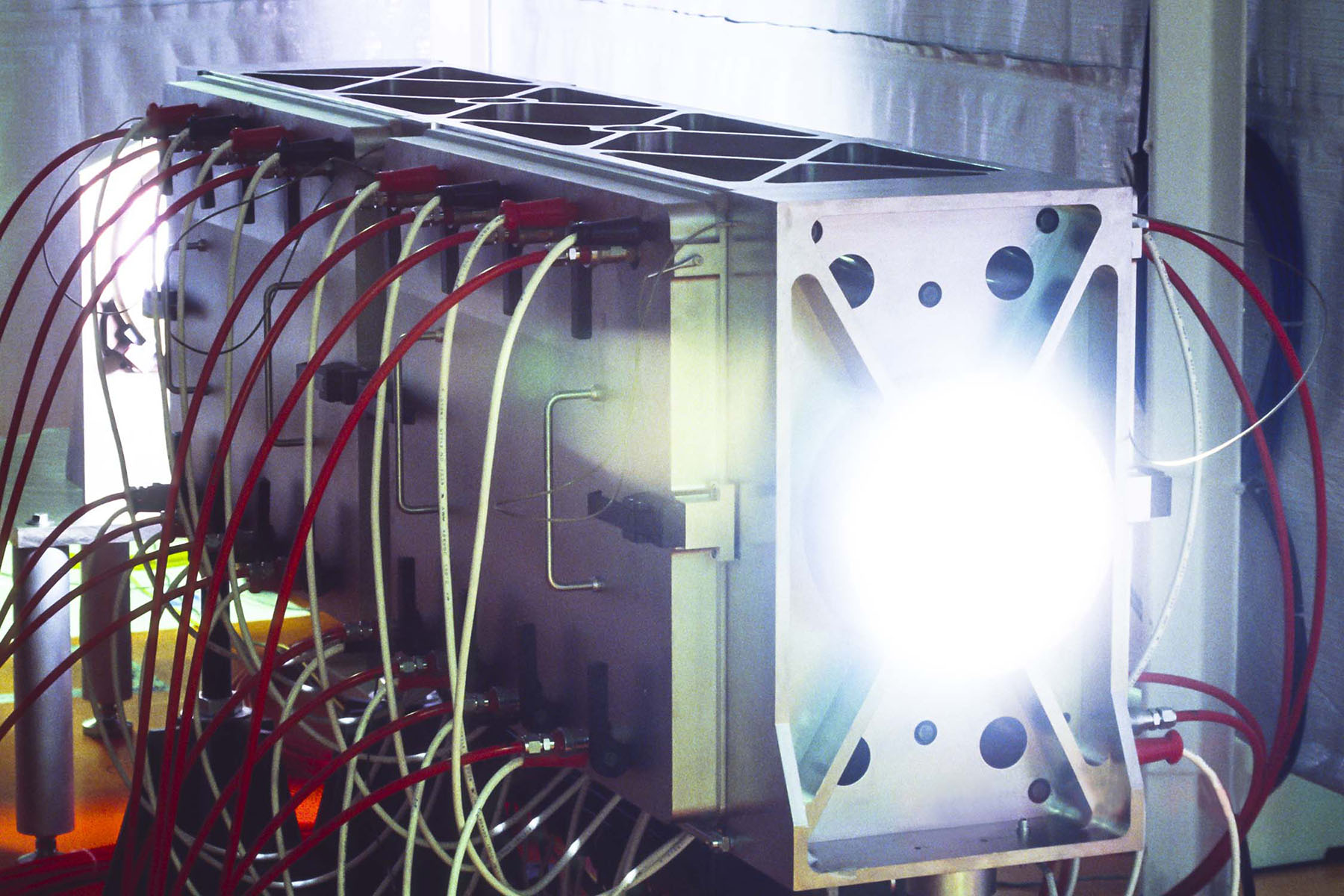 Bright light emits from a circular component at one end of a rectangular amplifier box, which has multiple cables connected.