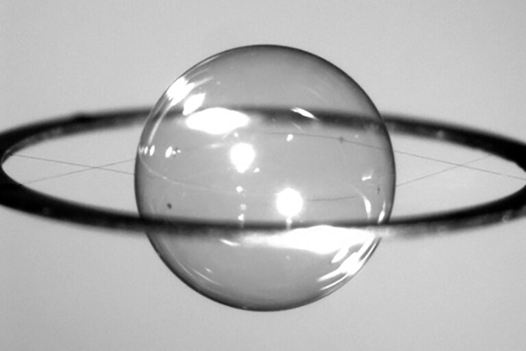 A transparent sphere being held by thin thread appearing to be floating in the middle of a ring.
