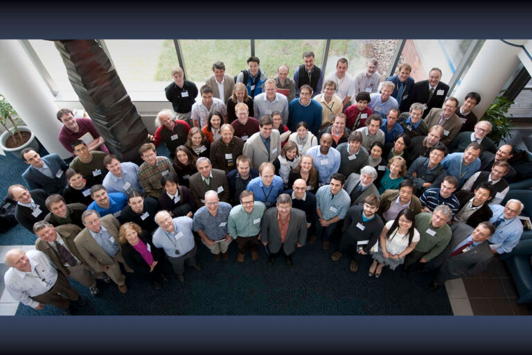 Photo of a group of approximately 65 people taken from above. The group looks up at the camera and smiles.