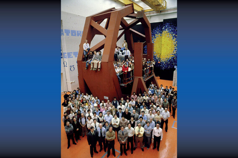 Large group photo of facility staff gathered around and on a massive geometric support structure inside a laser laboratory bay.