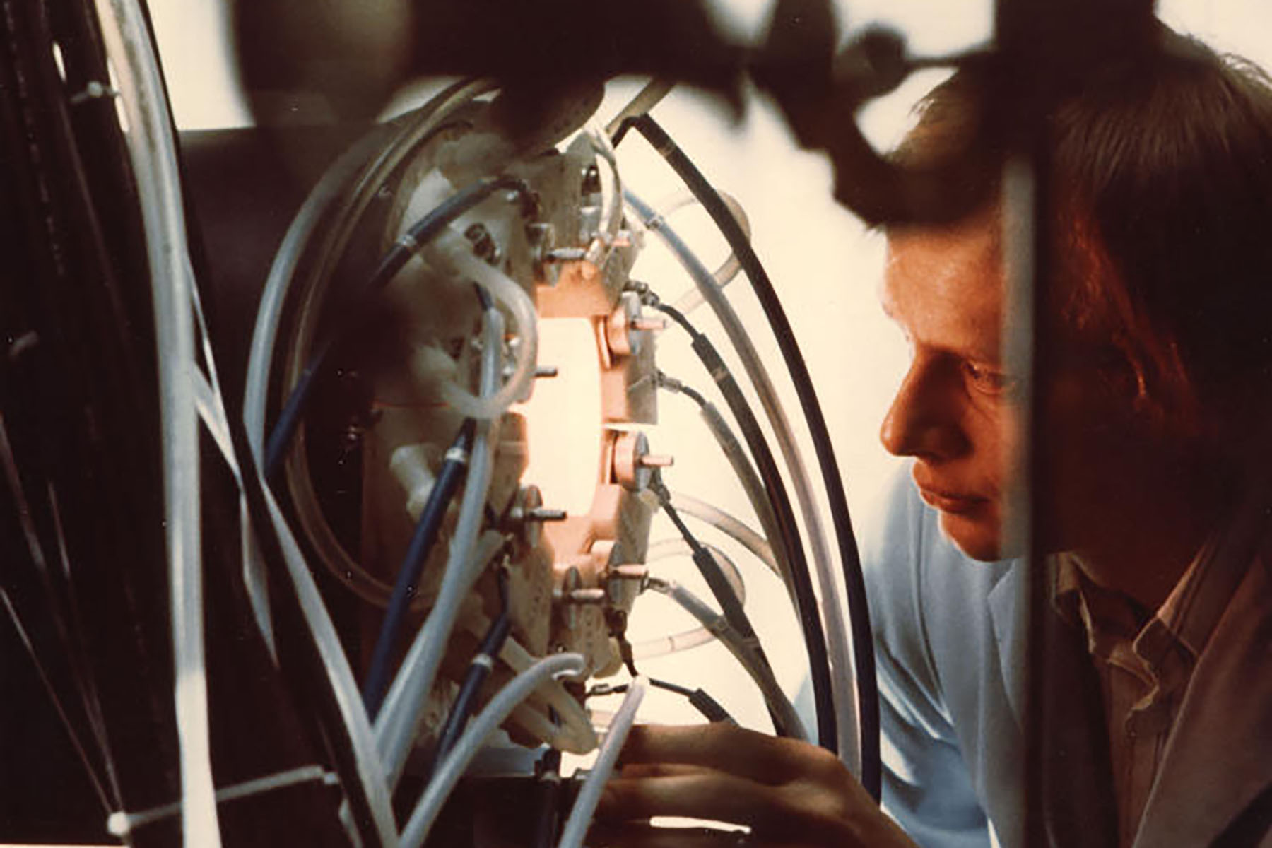 Researcher adjusting a plasma or laser diagnostic assembly with numerous attached cables and tubing.