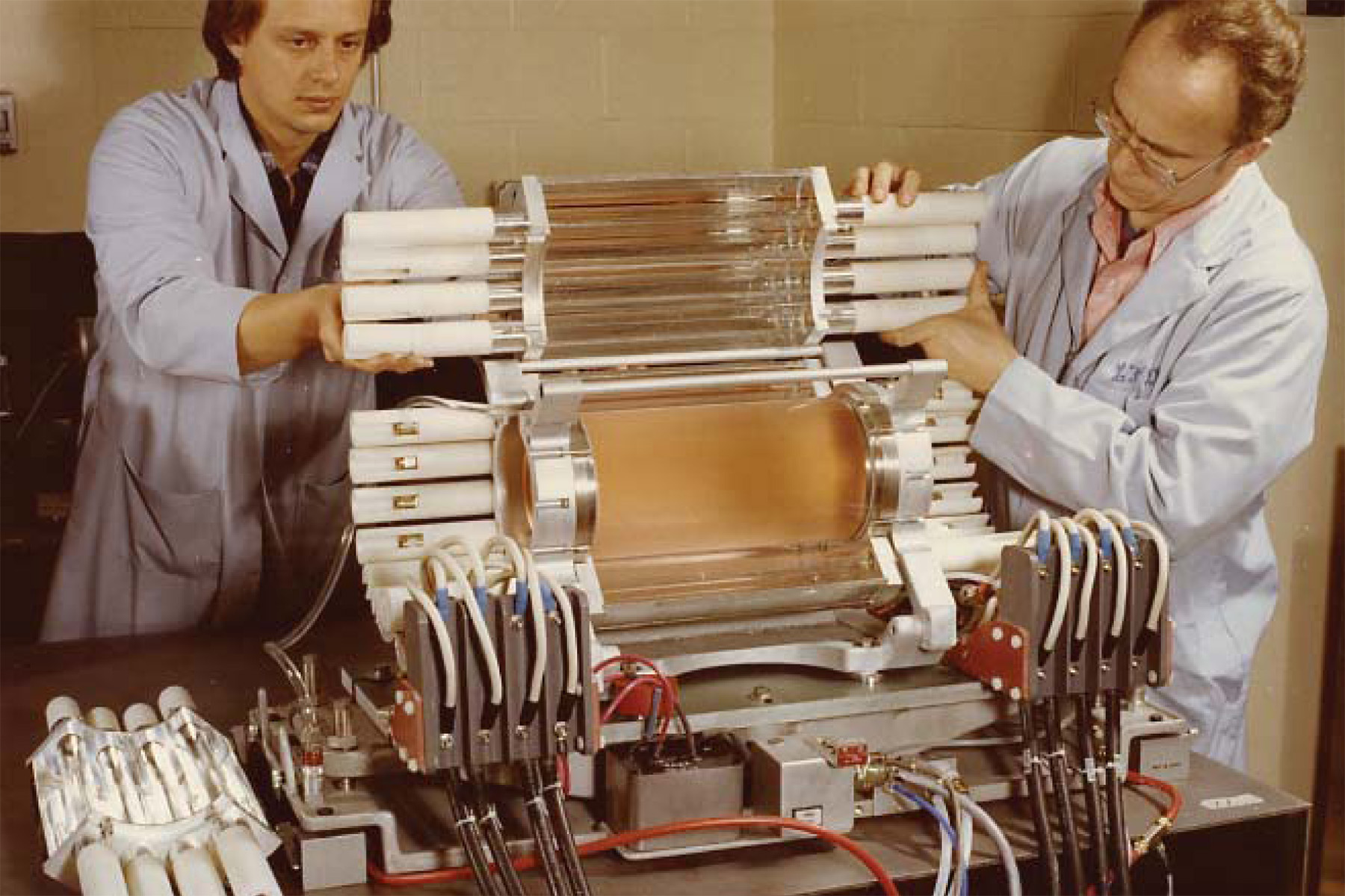 Researchers working with a large cylindrical laser or diagnostic assembly connected to multiple cables and control components.