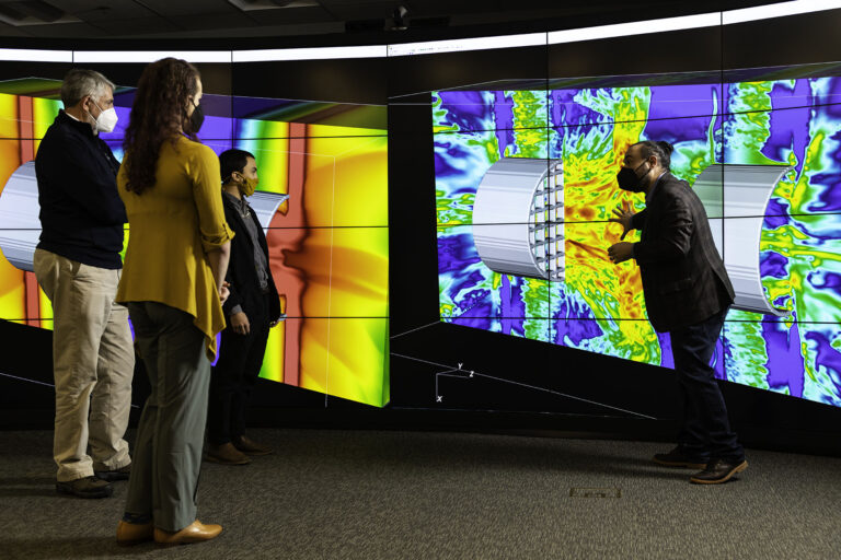 People viewing large, colorful scientific visualizations displayed on wall-sized screens in an immersive visualization room.