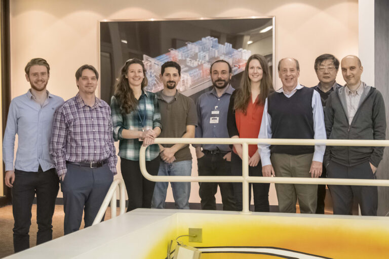 Group of people posing in front of a poster smiling.