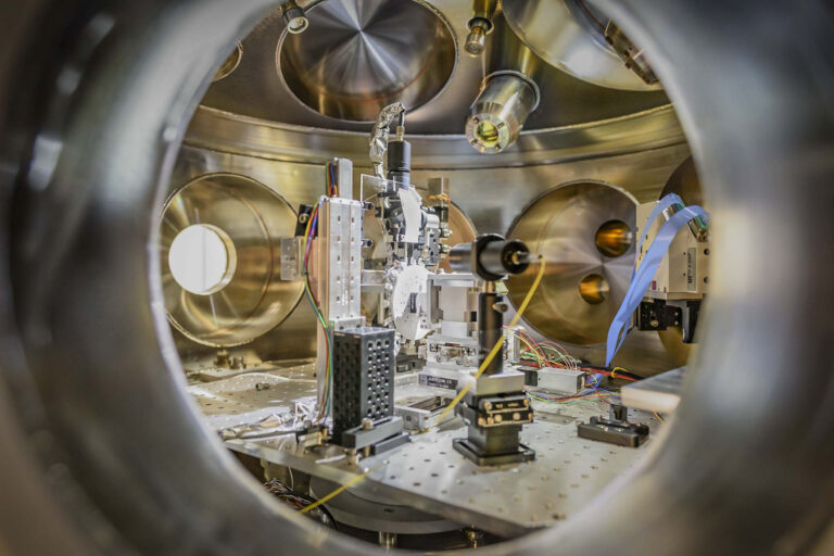 View inside a metallic vacuum chamber showing precision scientific instruments, optics, and diagnostic components.