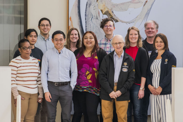 Group photo of several people standing together in a lab or office environment, smiling at the camera.