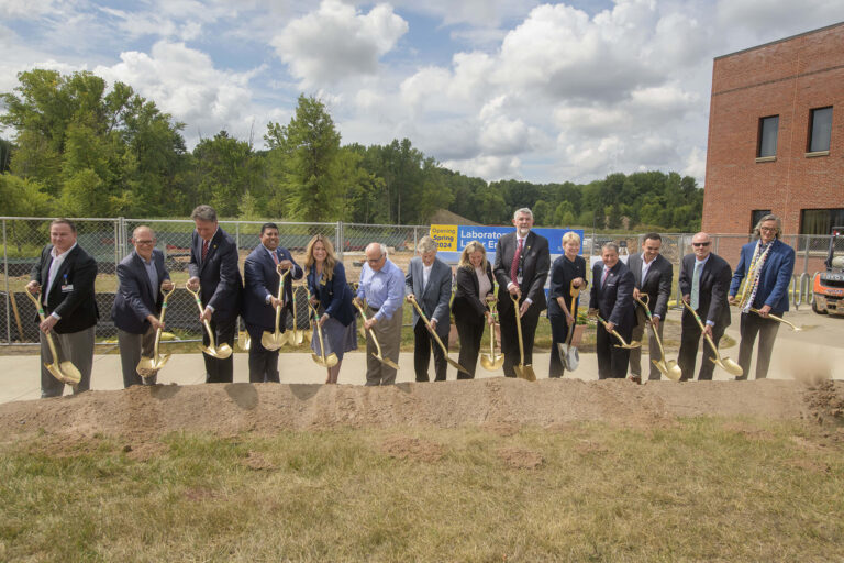 A group of officials and participants lined up outdoors holding shovels during a ceremonial groundbreaking event.