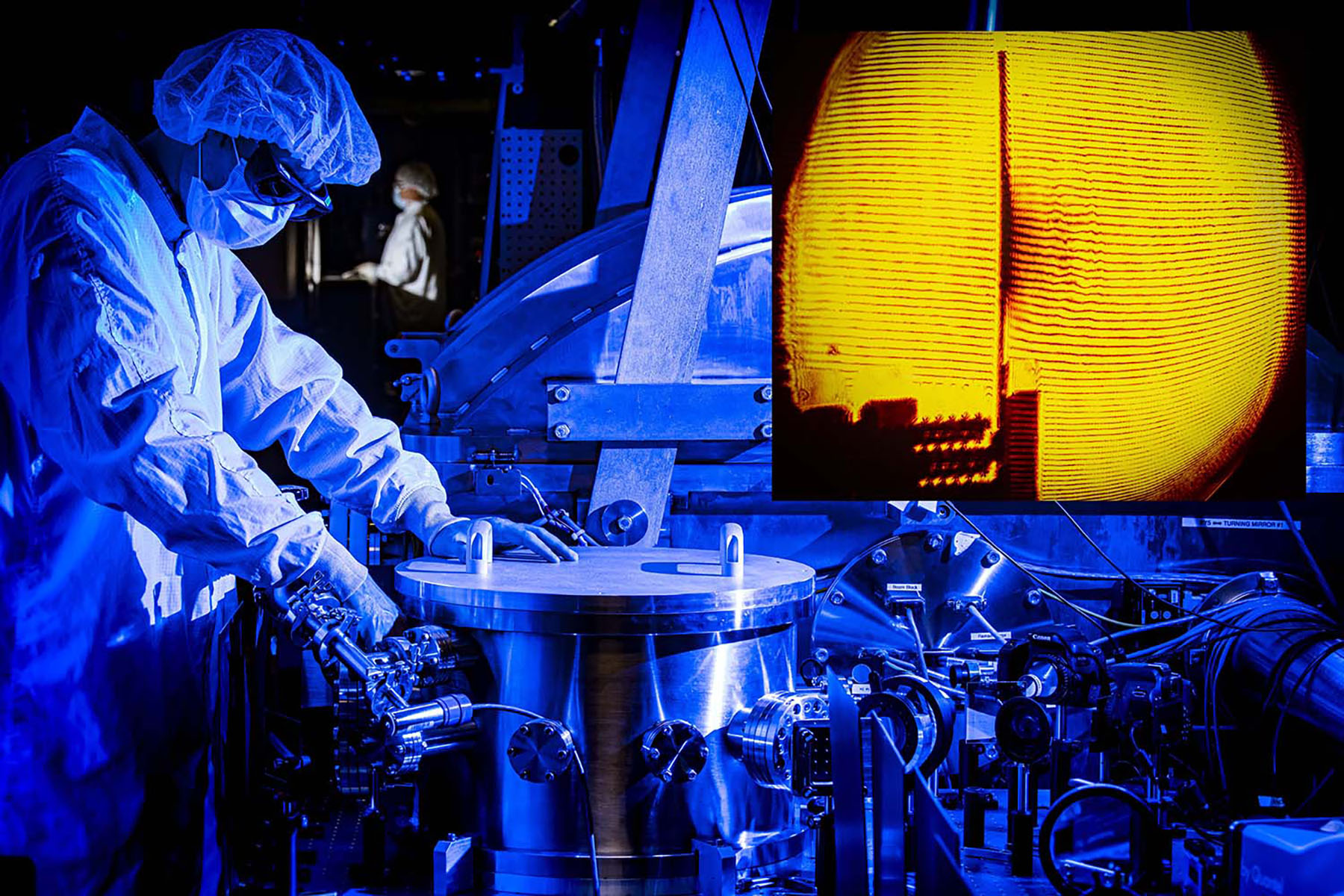 A technician in cleanroom gear working on a laser experiment illuminated by intense blue light, with a glowing yellow diagnostic screen in the background.