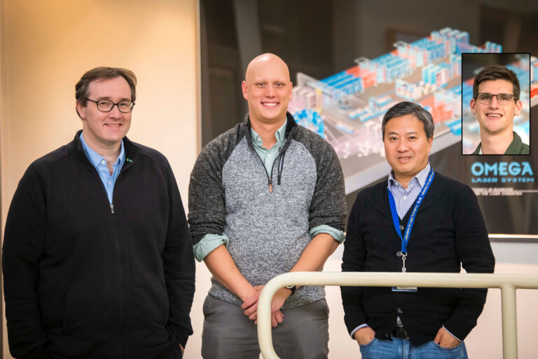 Three people standing indoors in front of a large scientific poster, smiling toward the camera.