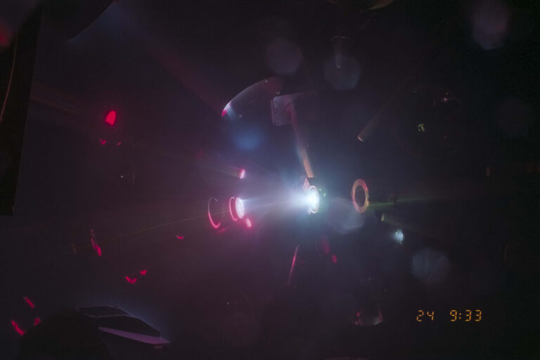 Dimly lit laboratory scene with bright red and white laser beams illuminating equipment