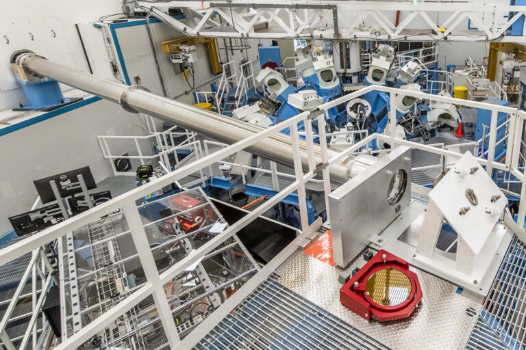 Large experimental facility interior showing walkways, pipes, and cables surrounding high-energy laser or fusion equipment.
