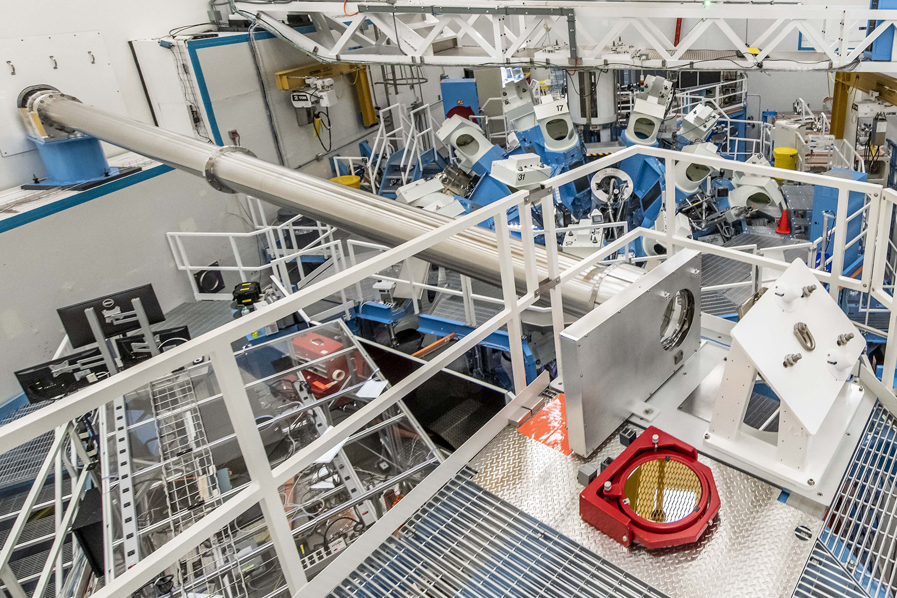 Large experimental facility interior showing walkways, pipes, and cables surrounding high-energy laser or fusion equipment.