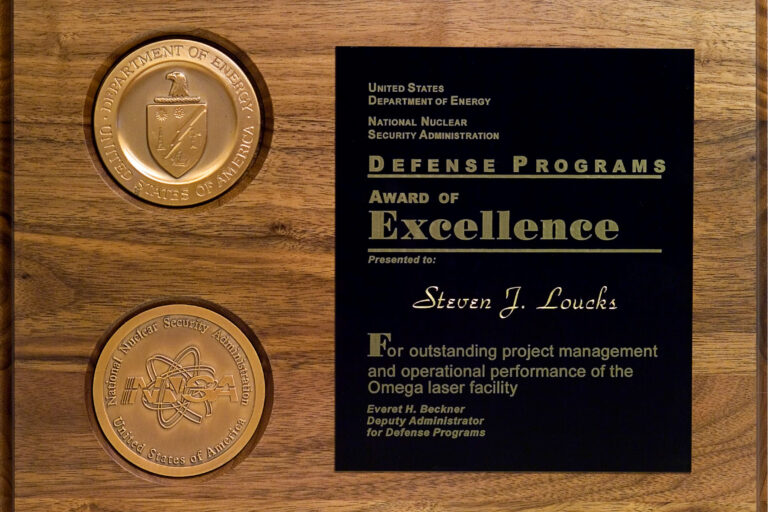 A wooden plaque with two medallions and a black overlay with writing.