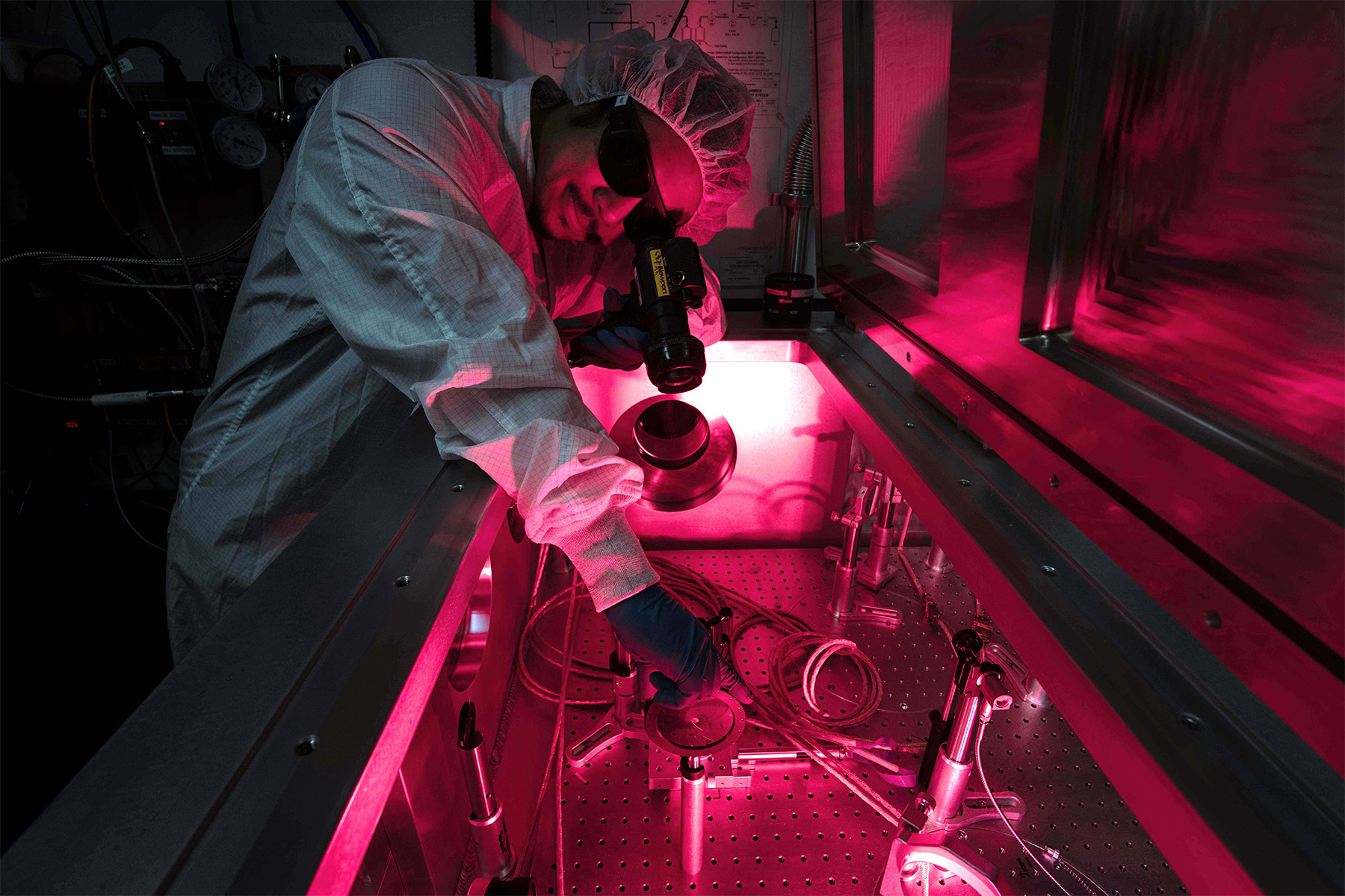 Student in cleanroom gear working on equipment in a laboratory.