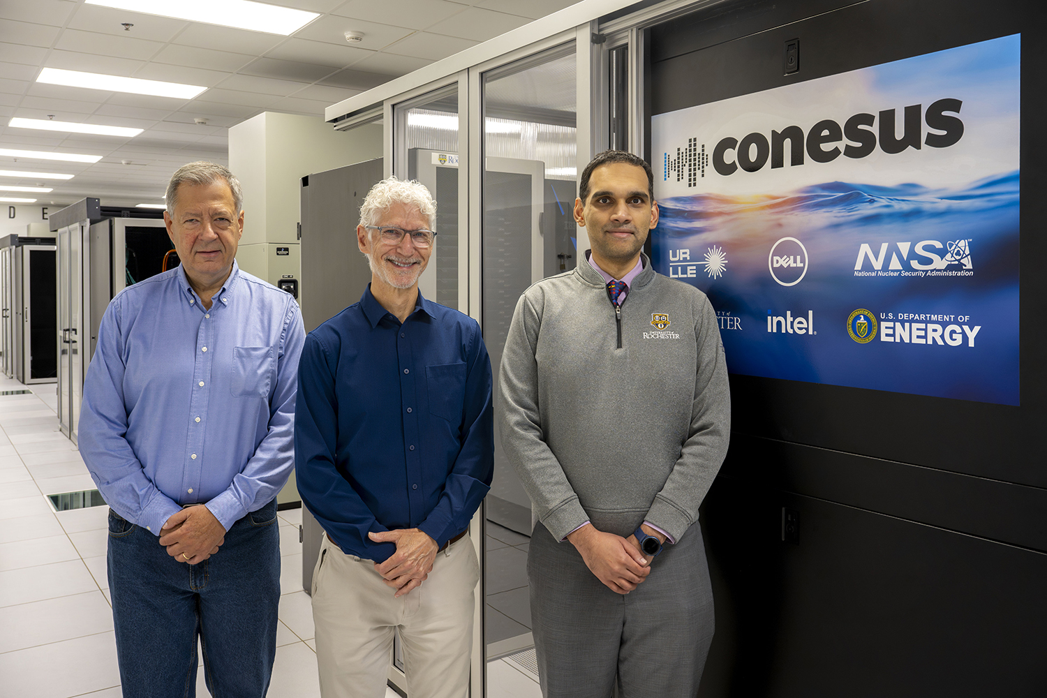 Group photo of Riccardo Betti, Mark Guardalben, and Varchas Gopalaswamy standing in front of Conesus computer cluster at the University of Rochester’s Primary Data Center.